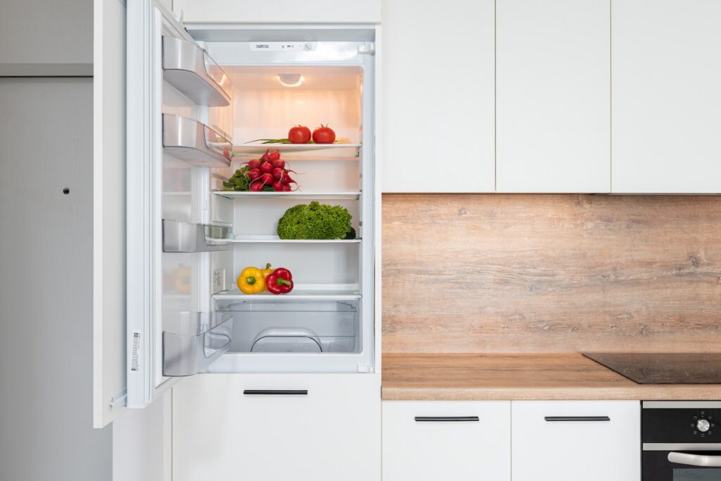 An open fridge door with vegetables in a kitchen